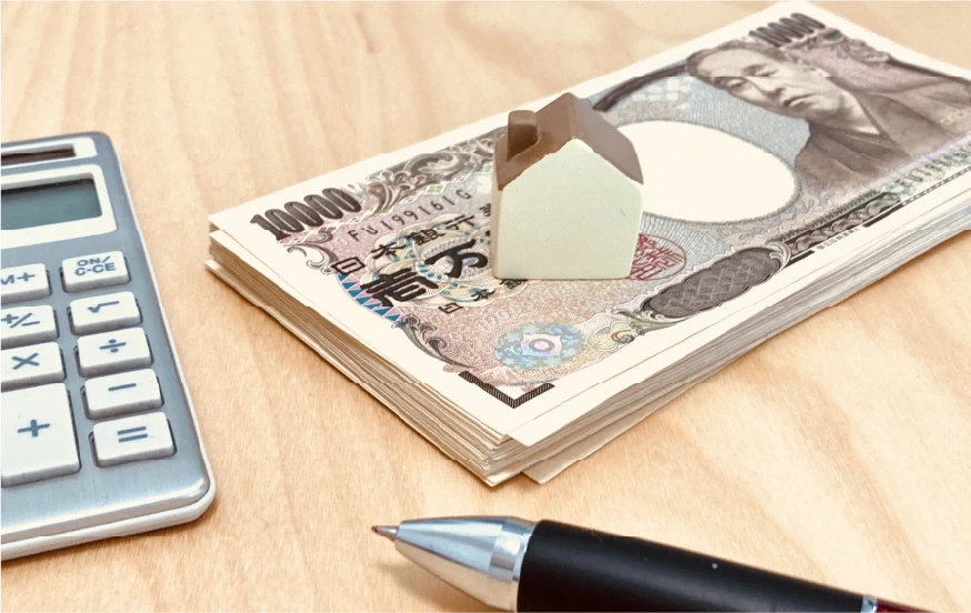 家とお金と計算機とペンの写真